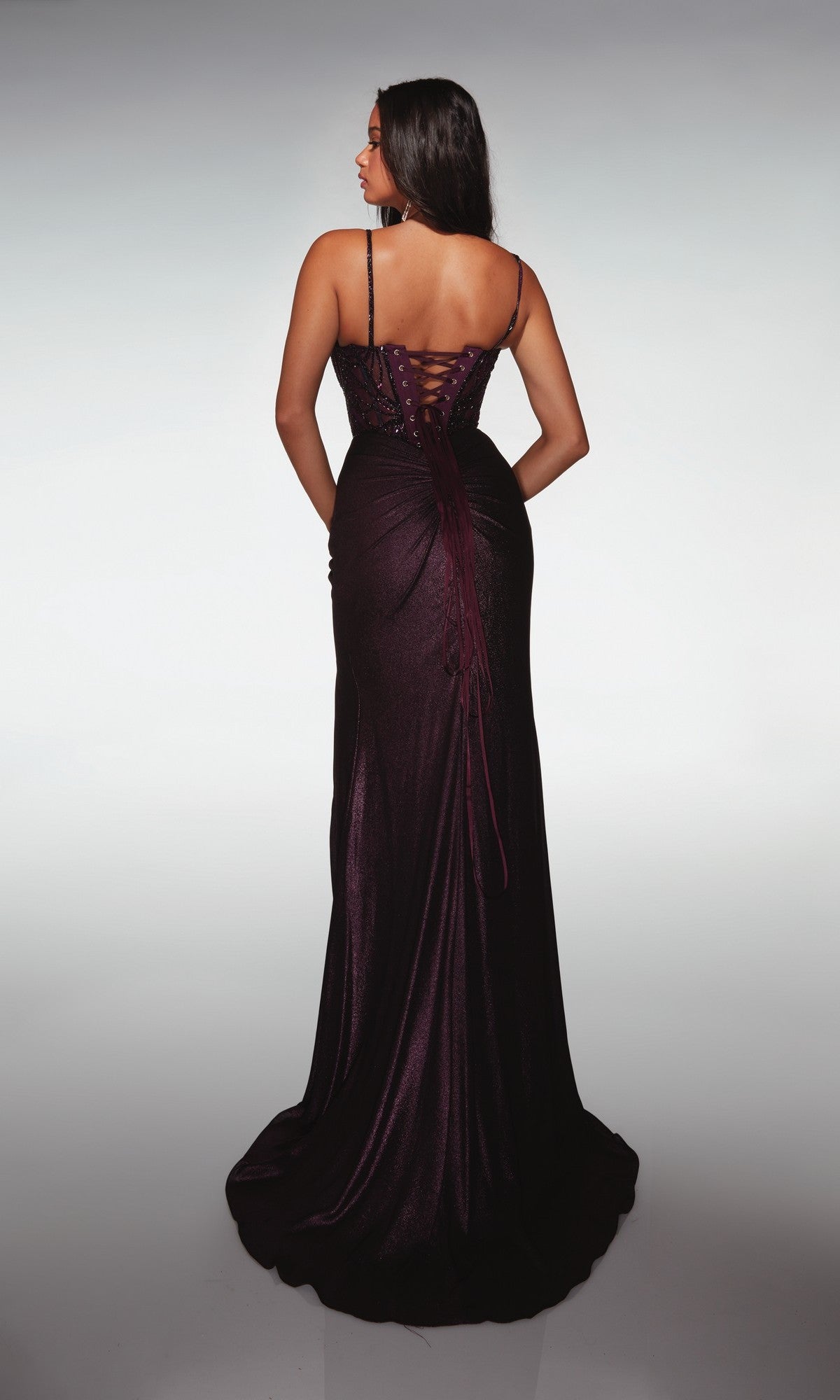 A woman stands with her back to the camera in the Alyce 62143 long formal dress, featuring a floor-length dark purple skirt, an embellished corset bodice, and lace-up back, set against a neutral background.